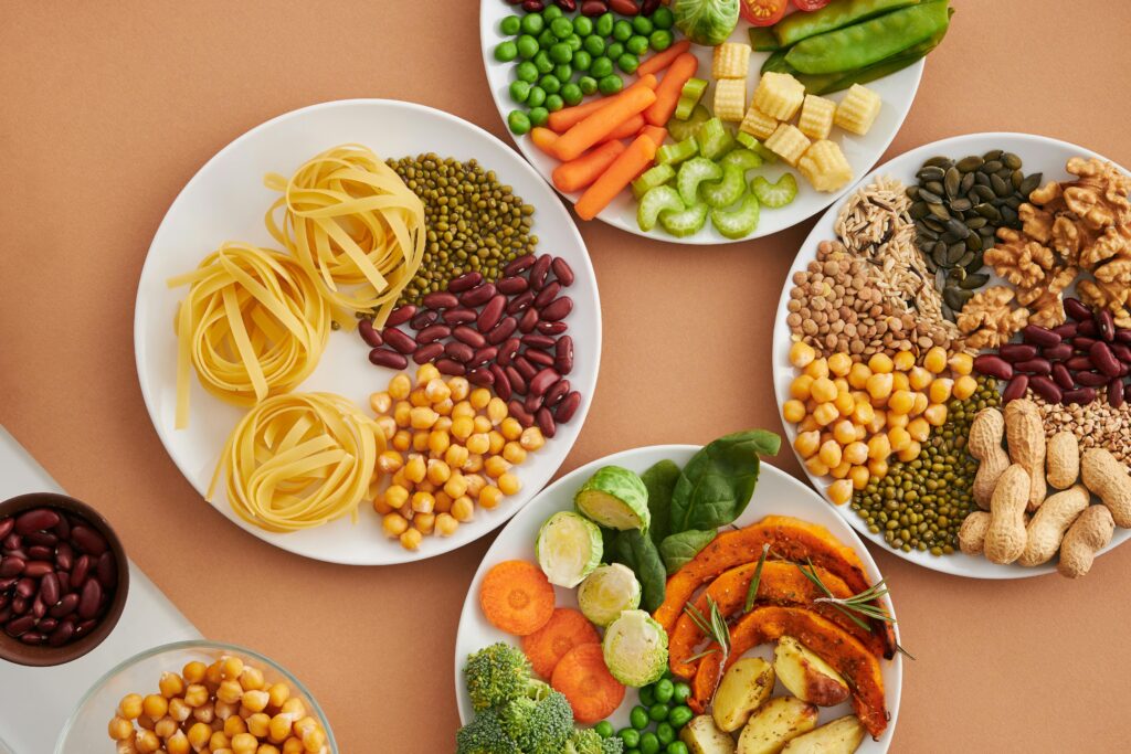 A vibrant mix of legumes, vegetables, nuts, and pasta arranged on white plates showcasing a balanced, healthy diet.